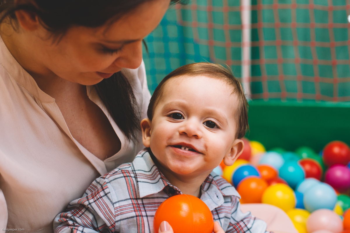 Aniversariante sorrindo dentro da piscina de bolinhas no colo da mãe