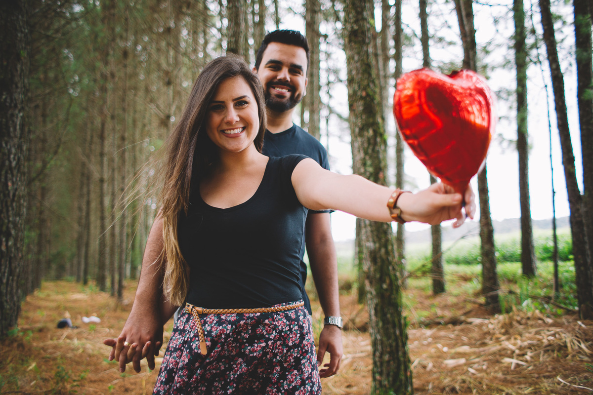 Casal de mãos dadas entre as árvores e a namorada segurando um balão vermelho