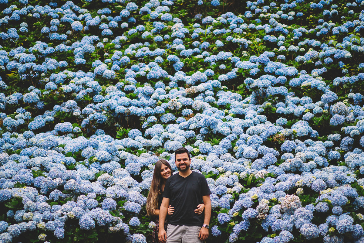 Casal abraçado em frente uma parede de flores hortênsias
