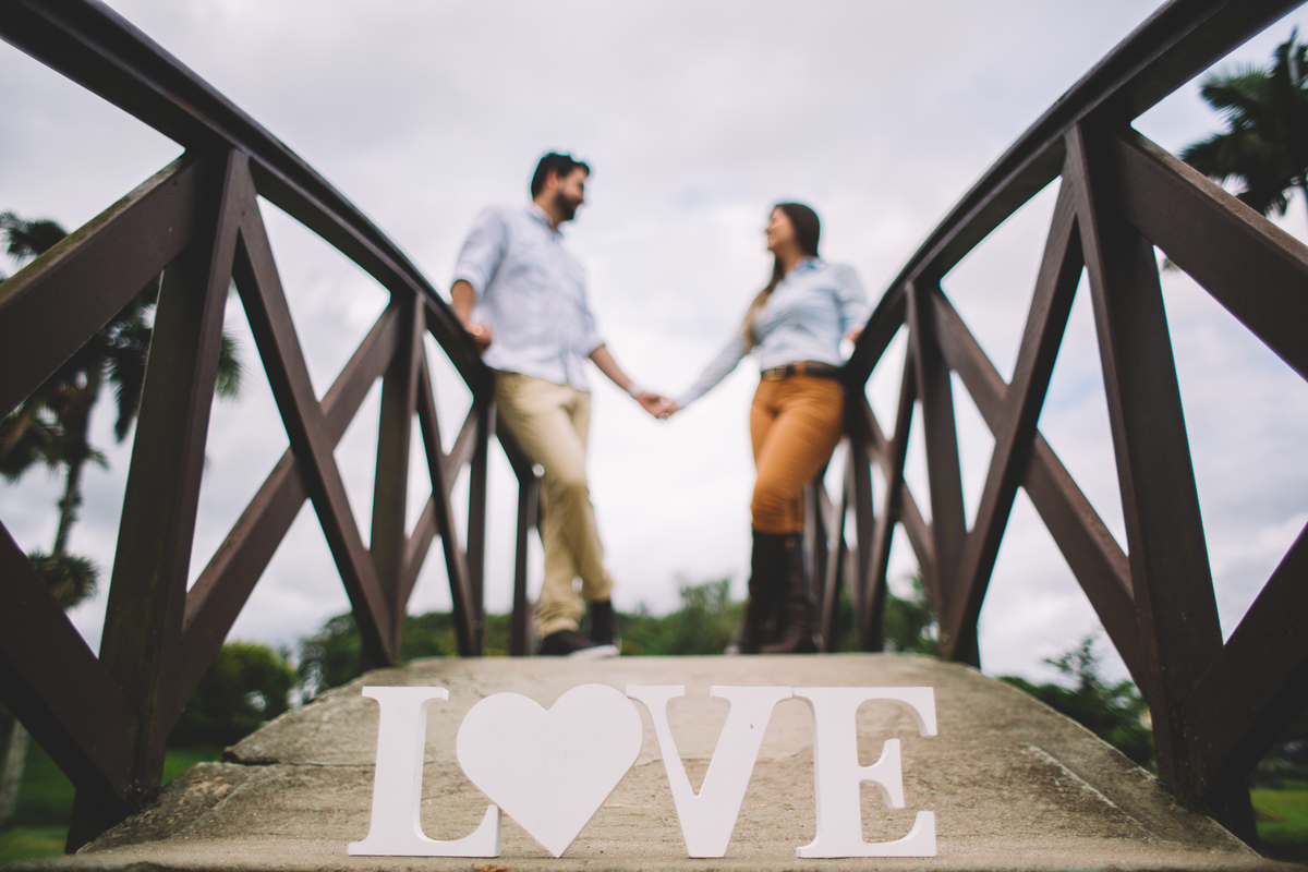 Casal de mãos dadas se apoiando na ponte com foco nas letras de LOVE no chão