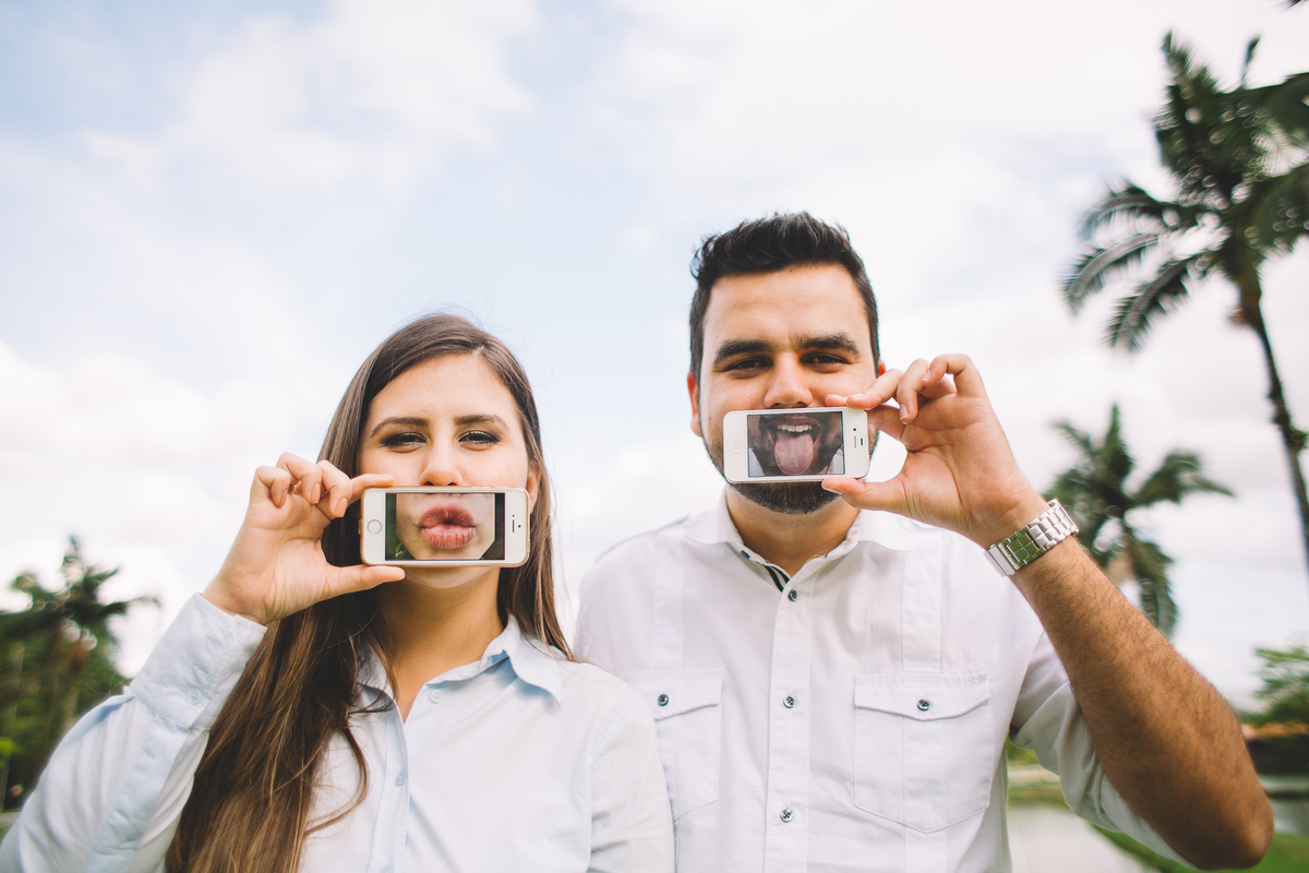 Foto divertida para ensaio pré wedding com os noivos segurando o celular na frente da boca e fazendo caretas