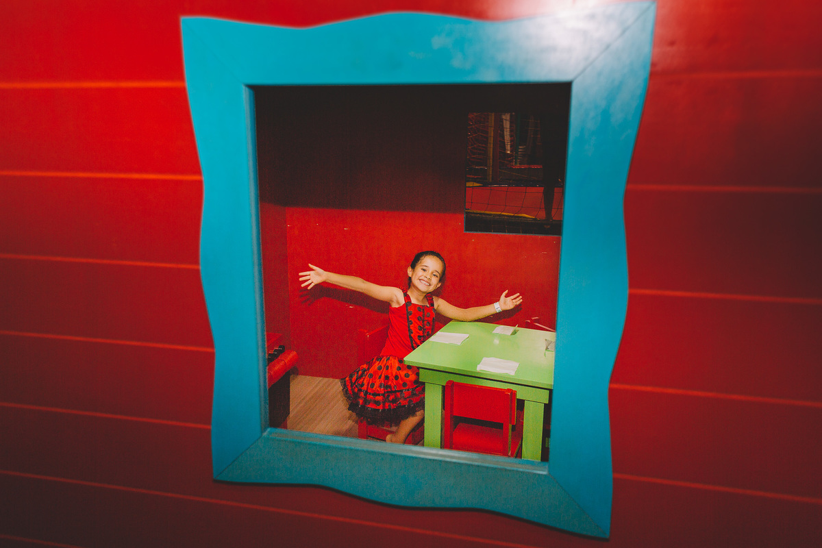 Criança brincando de casinha e sorrindo sentada com os braços abertos