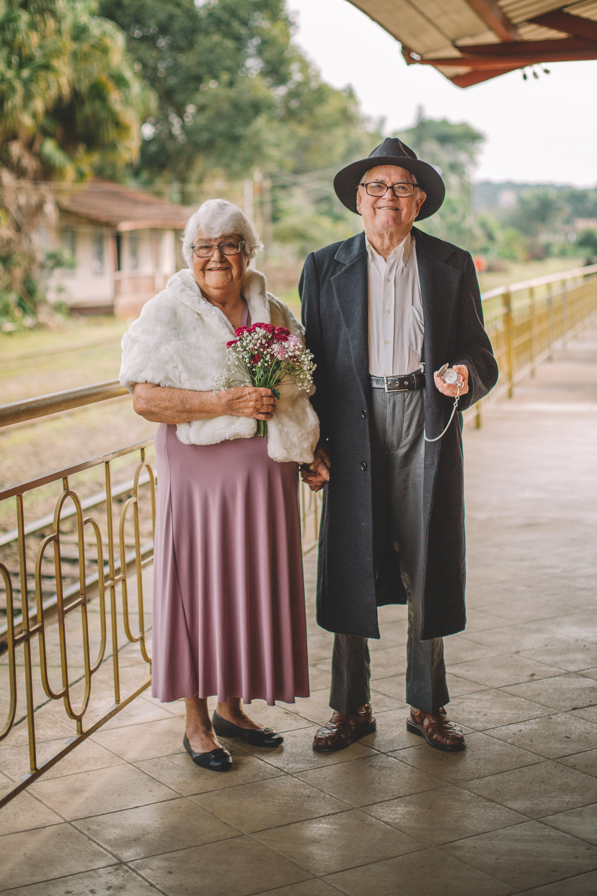 Dois velhinhos bem vestidos de mãos dadas em uma estação de trem