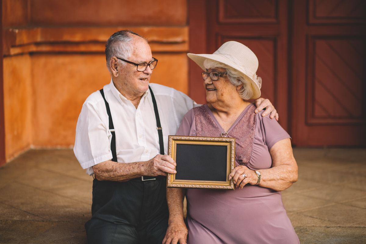 Foto do casal de idosos segurando um quadro e sorrindo um para o outro