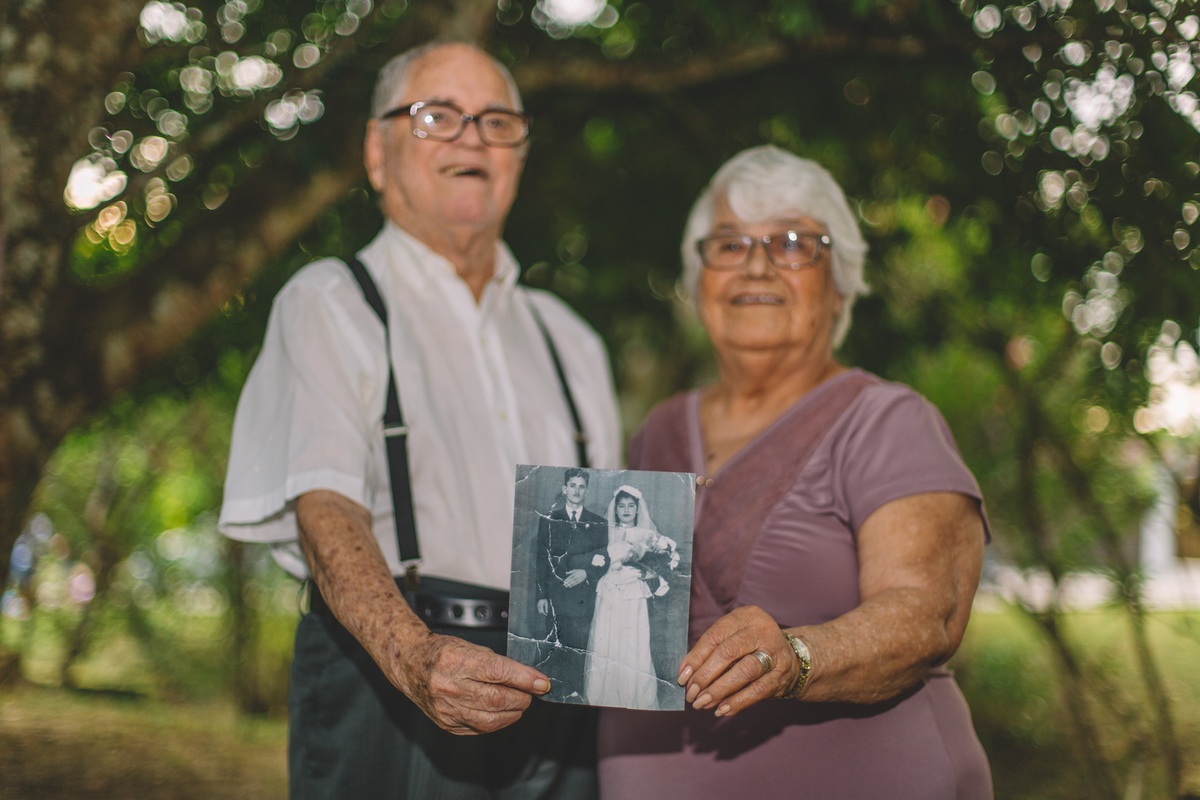 casal de velhinhos sorrindo e mostrando a foto antiga do seu casamento