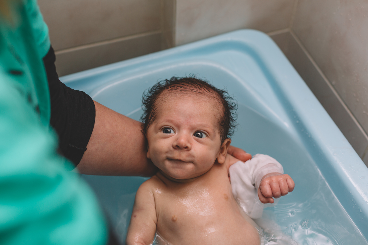 mamãe dando banho no bebê na banheira enquanto ele olha para ela com um sorriso