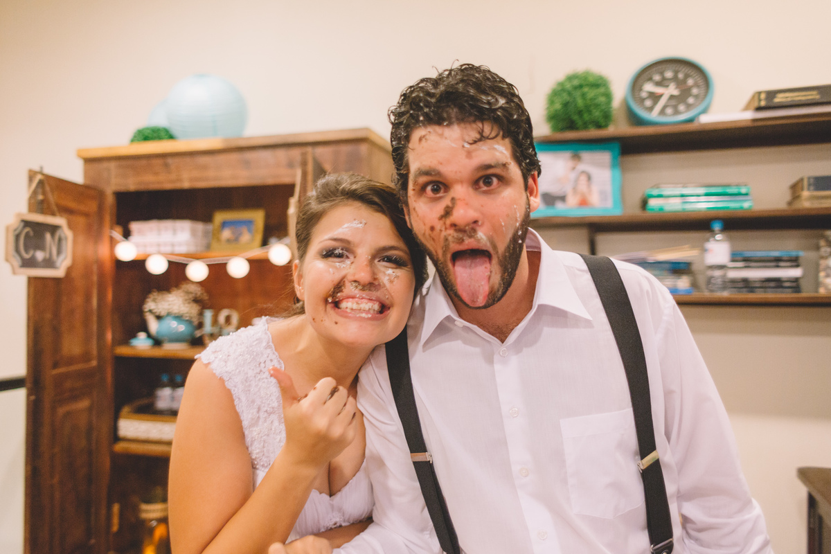 noivos com o rosto todo sujo de bolo sorrindo e mostrando a língua