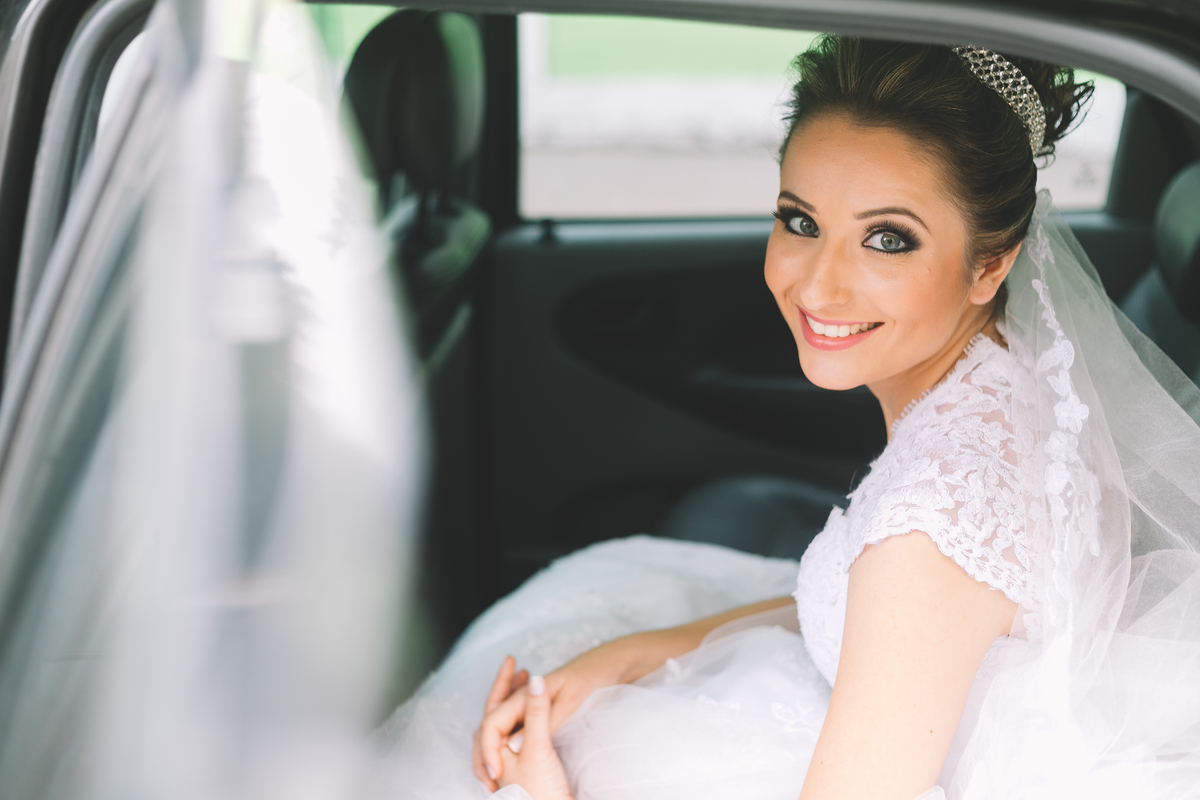 noiva sorrindo sentada no banco de trás do carro com a porta aberta