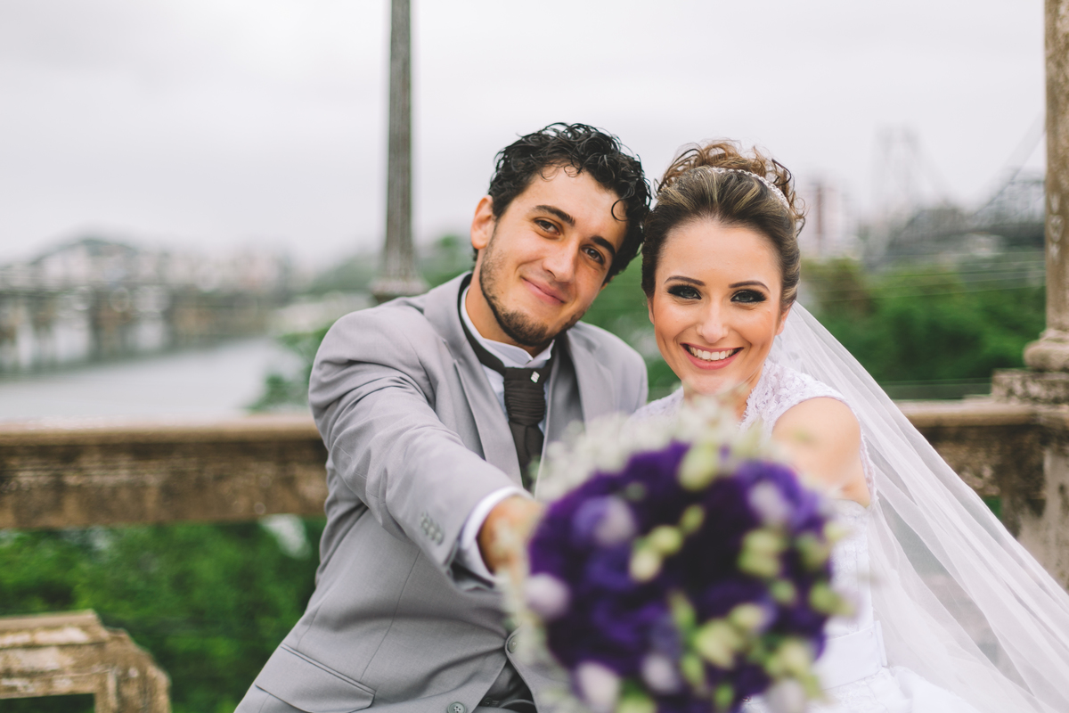 Noivos sorrindo apontando o buquê para a câmera