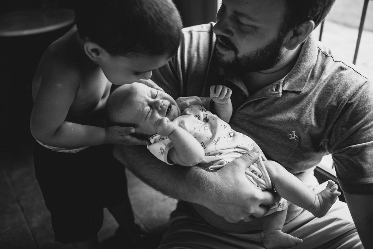 hermano besa la frente de su hermanito bebe, el padre los mira