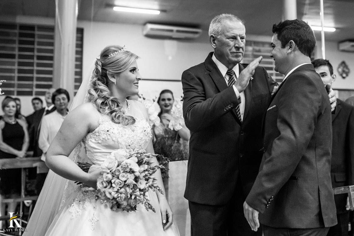 cerimonia de casamento heloisa e isaias em coronel vivida parana entrada da noiva com vestido branco e buquet seu pai cumprimenta o noivo e entrega sua filha fotografo katy tesser
