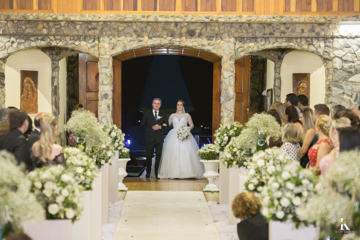 cerimonia religiosa de camila e fernando no santuario de nossa senha aparecida em laranjeiras do sul a decoração rosas brancas pajens com carrinho de bebe plaquinhas com mensagens e uma boneca com as alianças katy tesser fotografo