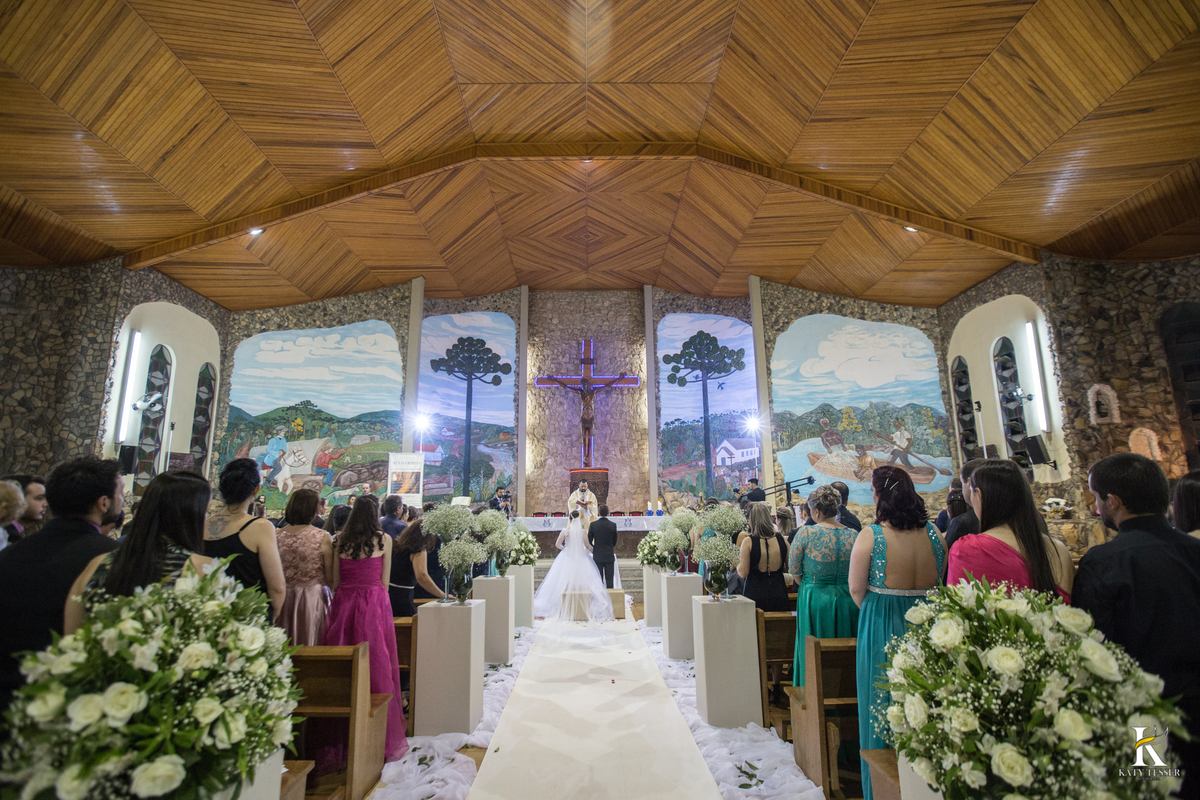 cerimonia religiosa de camila e fernando no santuario de nossa senha aparecida em laranjeiras do sul a decoração rosas brancas pajens com carrinho de bebe plaquinhas com mensagens e uma boneca com as alianças katy tesser fotografo
