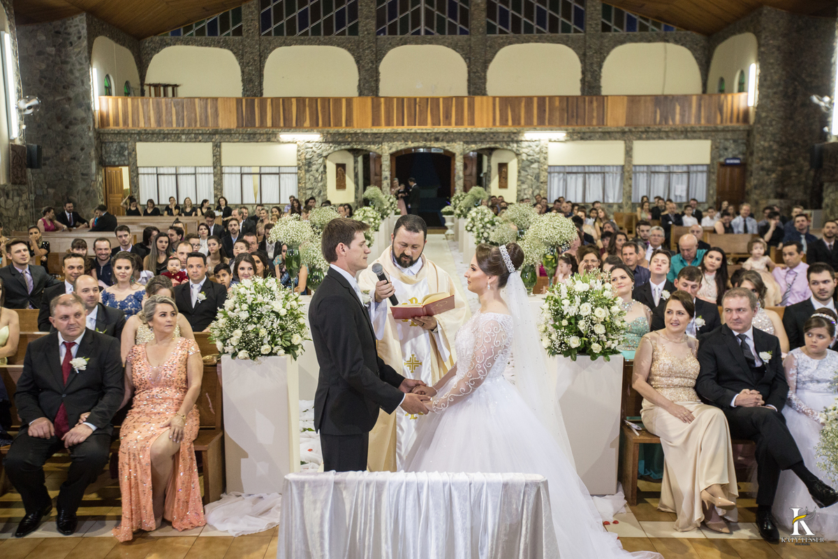 cerimonia religiosa de camila e fernando no santuario de nossa senha aparecida em laranjeiras do sul a decoração rosas brancas pajens com carrinho de bebe plaquinhas com mensagens e uma boneca com as alianças katy tesser fotografo
