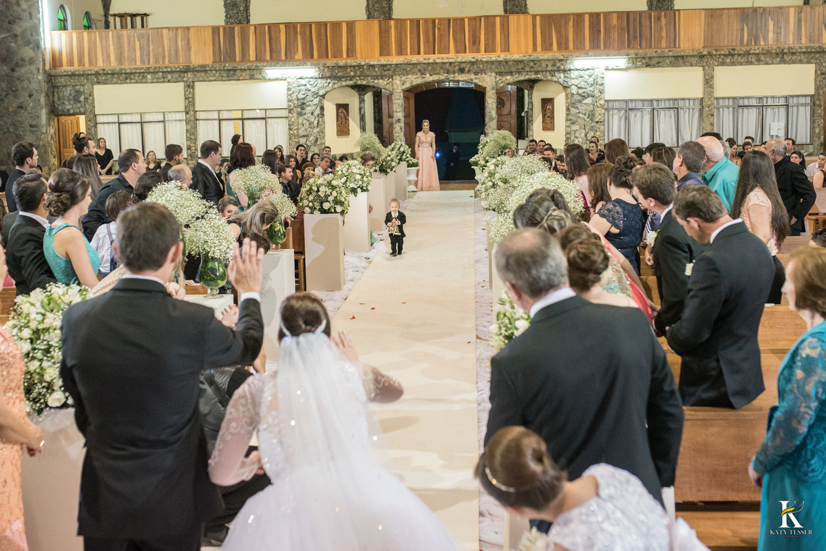 cerimonia religiosa de camila e fernando no santuario de nossa senha aparecida em laranjeiras do sul a decoração rosas brancas pajens com carrinho de bebe plaquinhas com mensagens e uma boneca com as alianças katy tesser fotografo