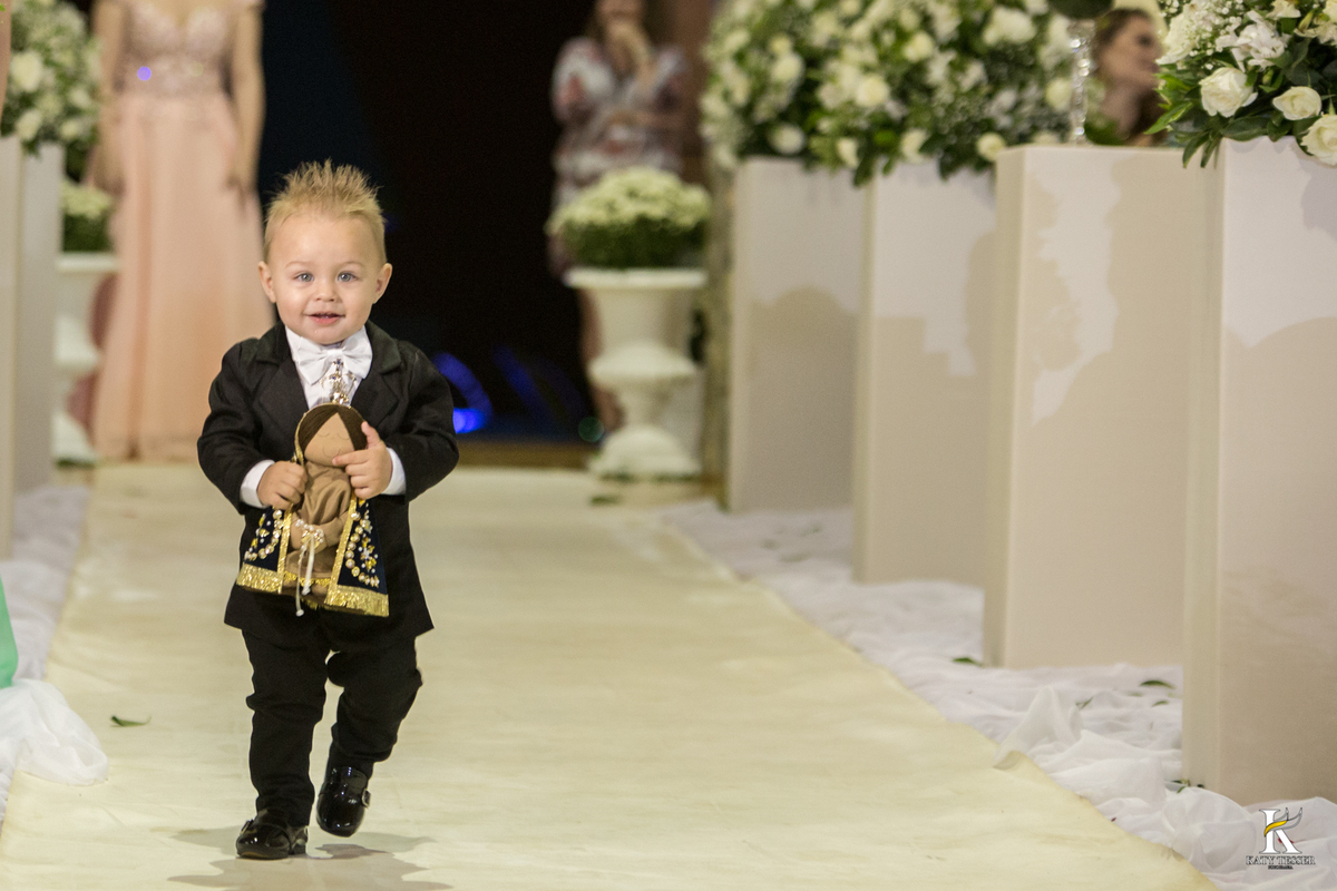 cerimonia religiosa de camila e fernando no santuario de nossa senha aparecida em laranjeiras do sul a decoração rosas brancas pajens com carrinho de bebe plaquinhas com mensagens e uma boneca com as alianças katy tesser fotografo