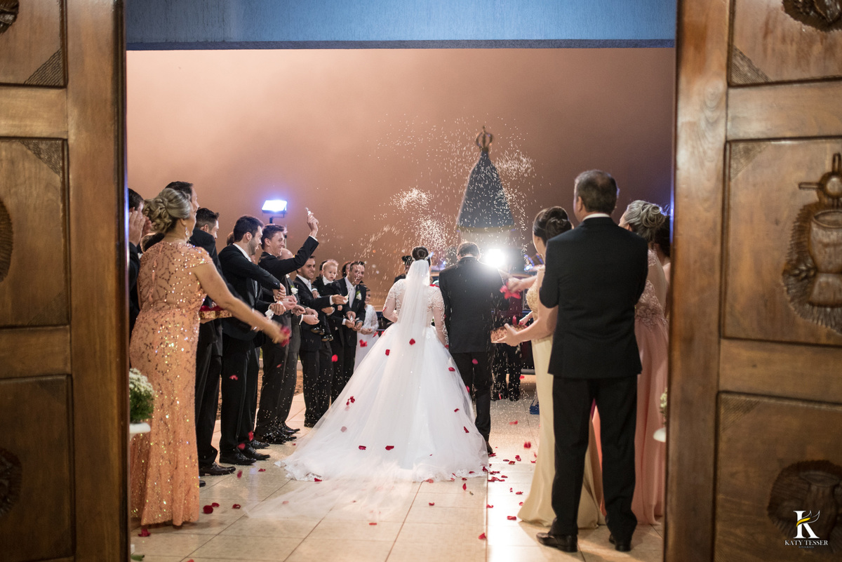 cerimonia religiosa de camila e fernando no santuario de nossa senha aparecida em laranjeiras do sul a decoração rosas brancas pajens com carrinho de bebe plaquinhas com mensagens e uma boneca com as alianças katy tesser fotografo chuva de arroz