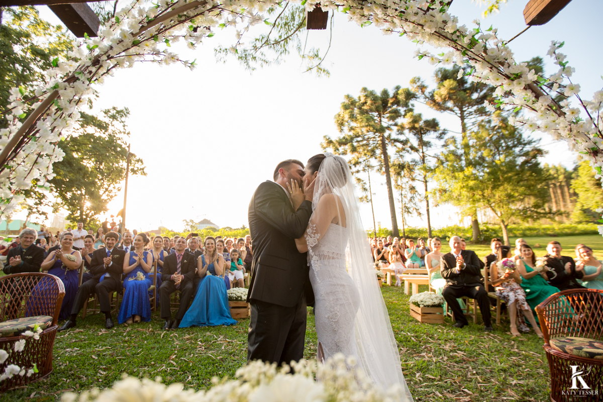 Casamento ao ar livre de dia na cabana manhare em Francisco beltrao parana de Ademir ana Paula as fotos de katy tesser fotografo na cerimonia no pergolado com flores com o primeiro beijos dos noivos