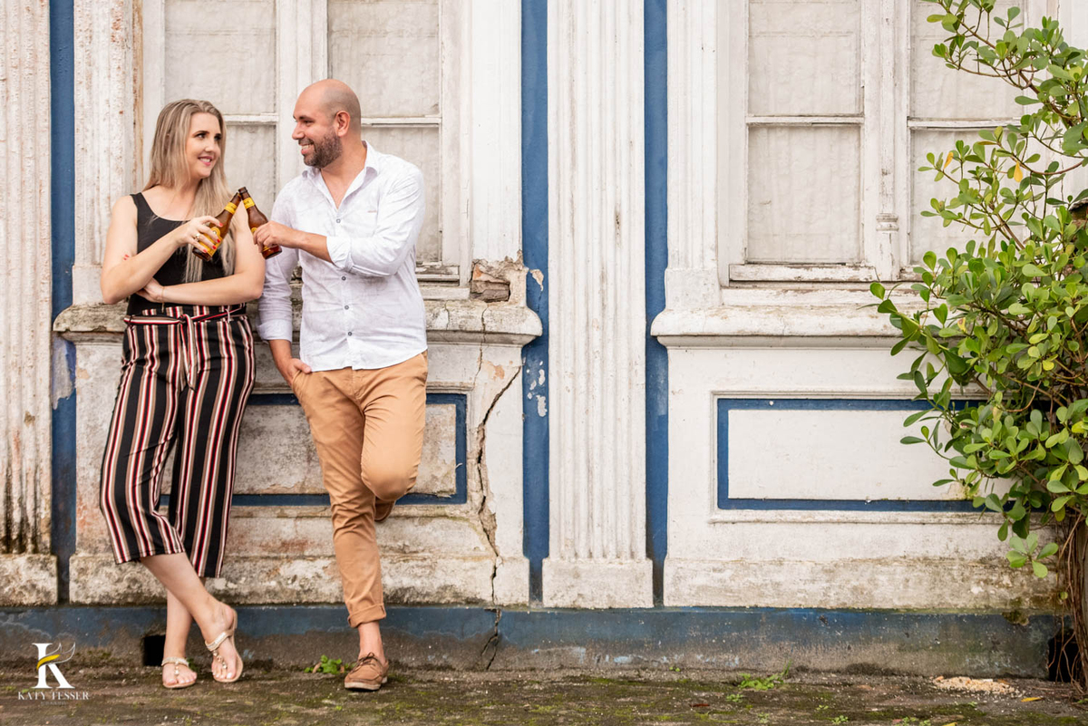 sessão book pre casamento de jessica e tiago em antonina e morretes no paraná com vestido de noiva branco vestido vermelho buque e cora de flores fotos externas ao ar livre katy tesser fotografa tomando cerveja