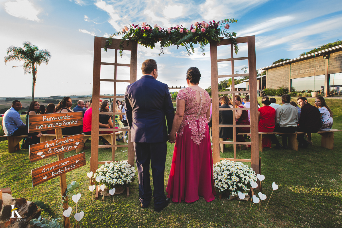 Casamento de ana Caroline e rodrigo em coronel vivida Paraná, casamento de dia ao ar livre com as madrinhas vestidas na mesma cor realizado por Katy Tesser fotografo entrada do noivo com a mãe numa moldura de porta decorada