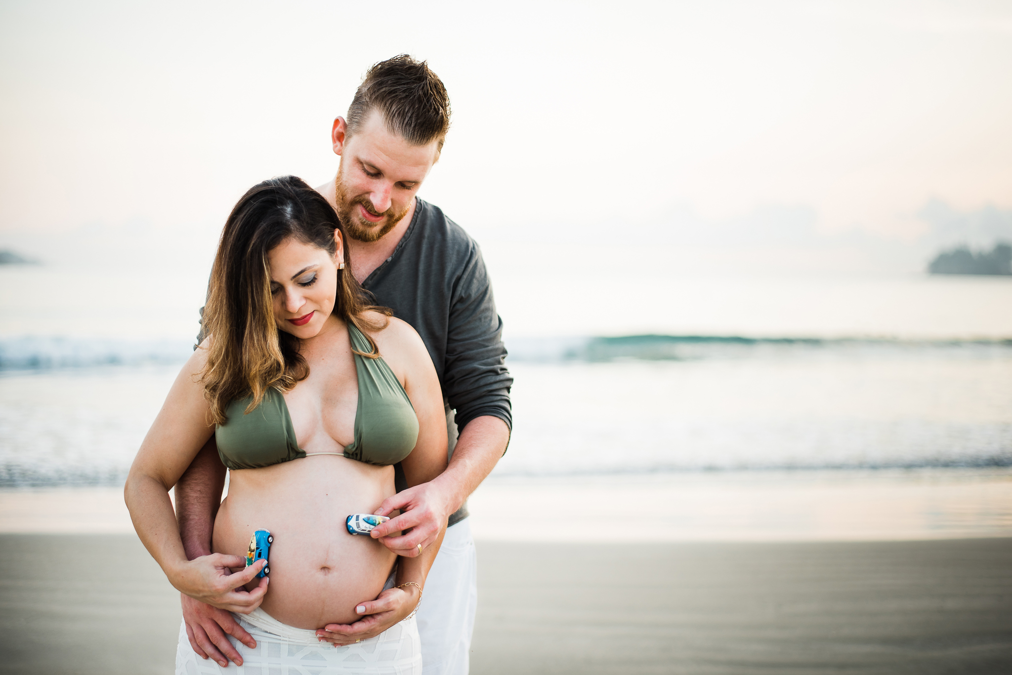Ensaio gestante praia do Guarujá casal feliz abraçados brincando com o carrinho