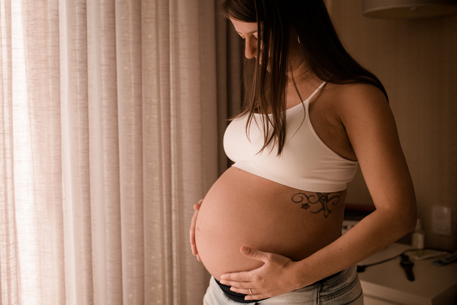 Mulher gestante olhando para barriga. Ensaio feito em casa.