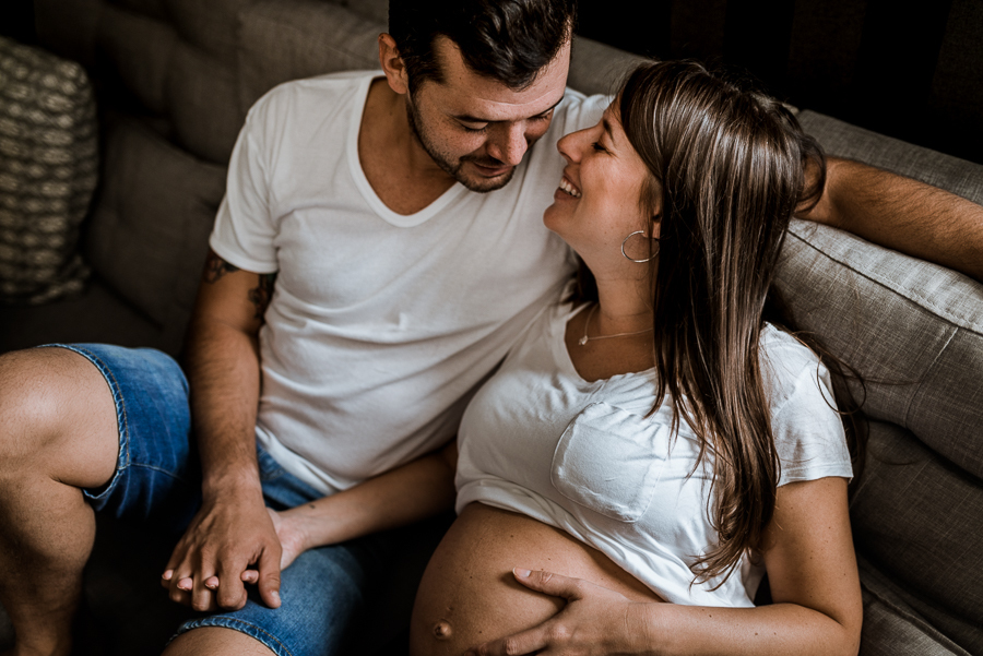 Casal no sofá de casa. Mulher gestante.