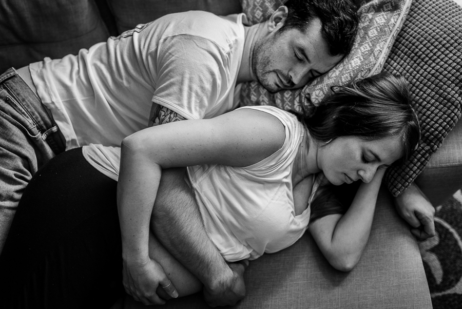 Casal deitado no sofá de casa. Mulher gestante.