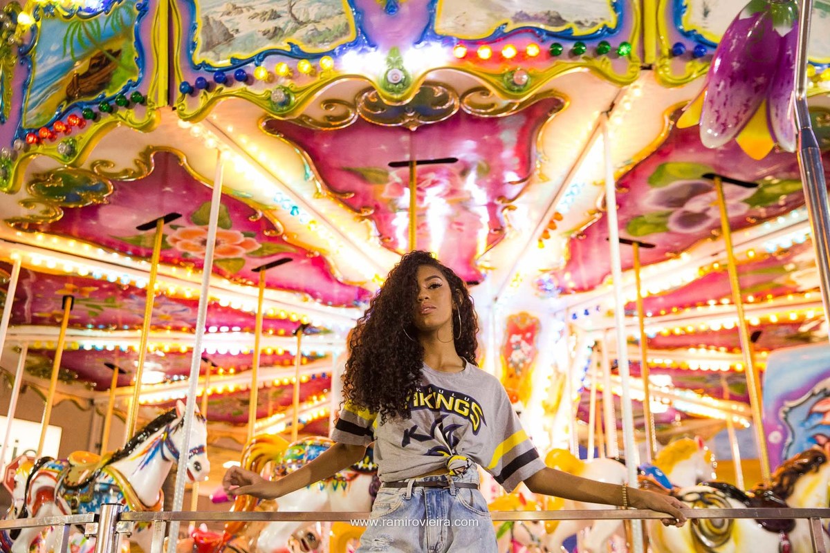 debutante posando para foto na frente de um carrossel no parque de diversão