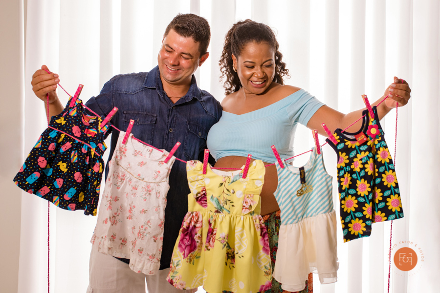 gestante com o papai segurando um varal de roupas do bebe