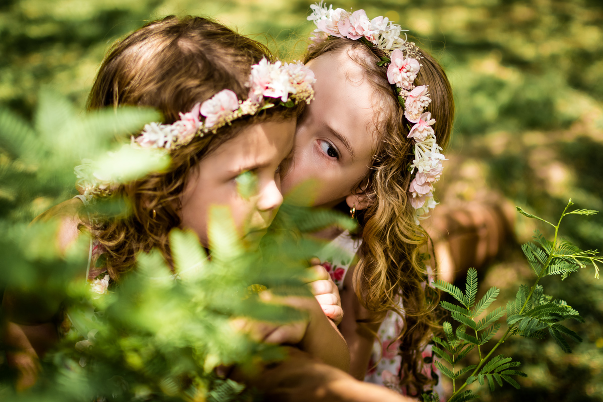 irmãs abraçadas e fazendo carinho uma a outra entre arbustos non rio 2 park posando pára ensaio infantil. Barra da Tijuca/RJ