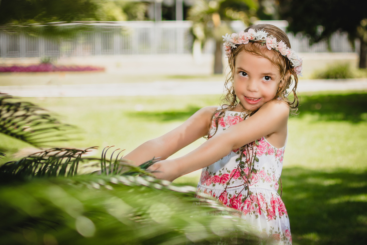 Isabella fazendo pose segurando um ramo de pequena palmeira durante o ensaio fotográfico infantil na Barra da Tijuca