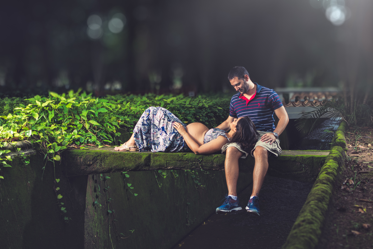 Aline deitada no colo do Márcio em pequena ponte sobre riacho, ensaio gestante no Jardim Botânico do Rio de Janeiro