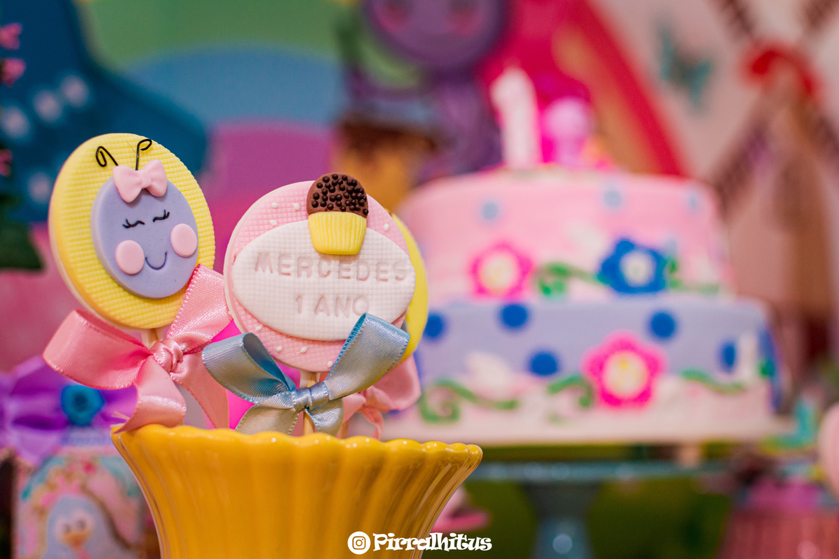 Detalhe dos pirulitos na mesa do bolo com o bolo desfocado no fundo, fotografia de aniversário infantil da Mercedes