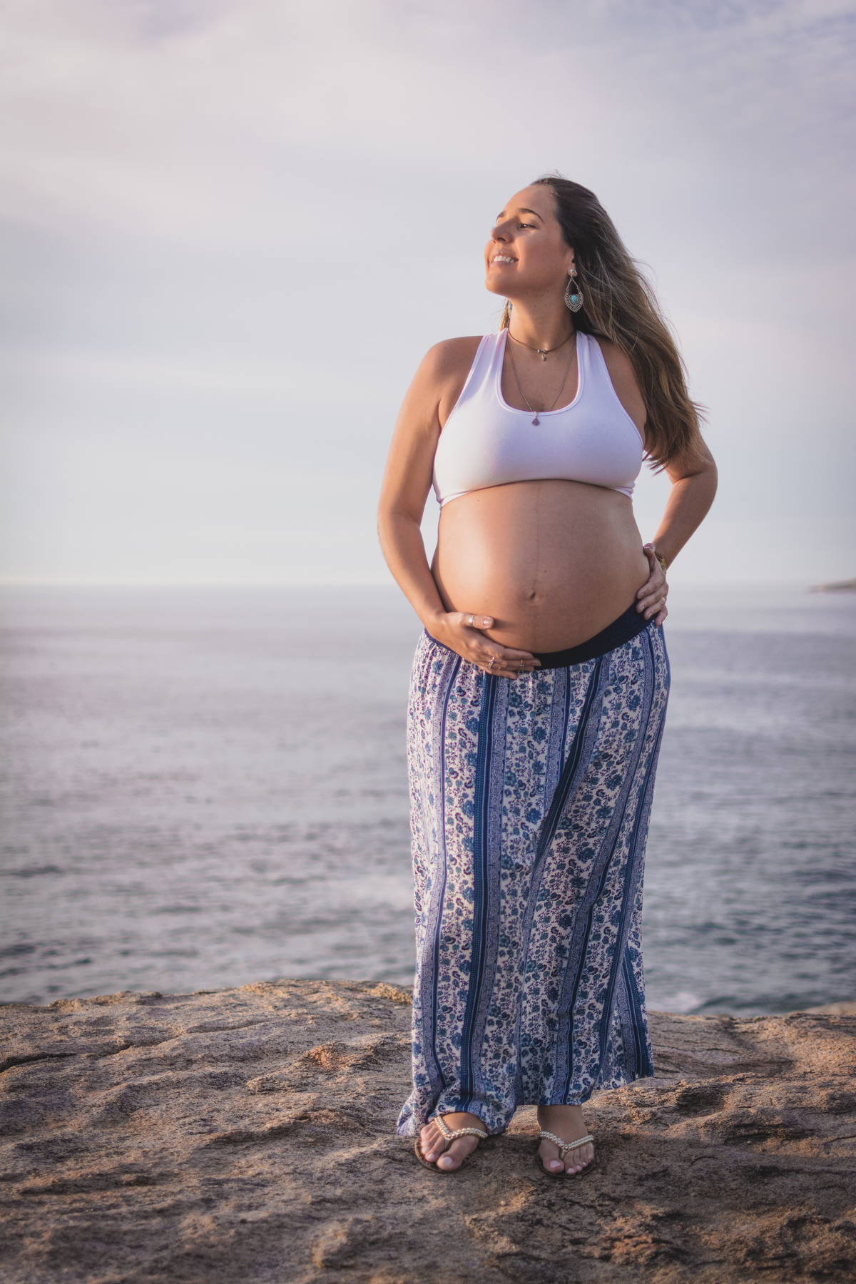 Linda gestante na praia de saia estampada e croped branco.
