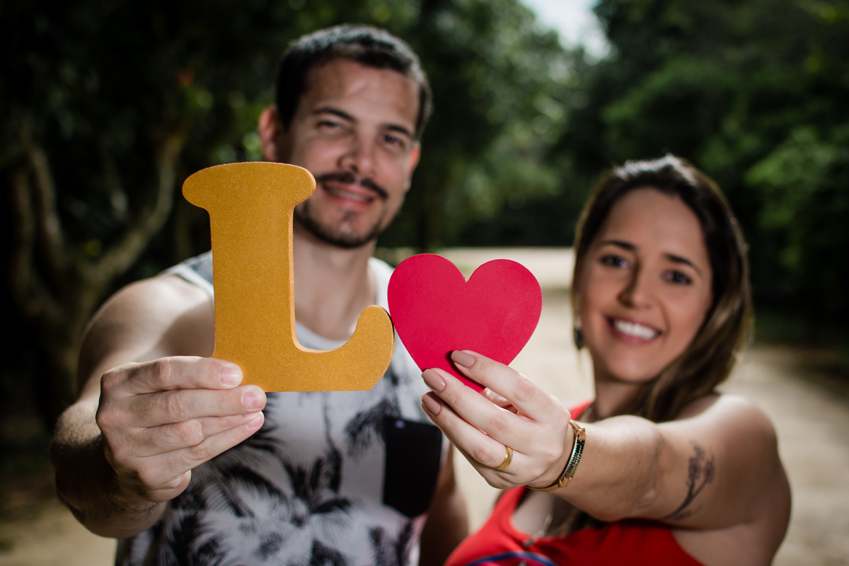 casal gestante segurando inicial do nome do bebê e um coração, ensaio realizado no Bosque da Barra, Barra da Tijuca / Rio de Janeiro.