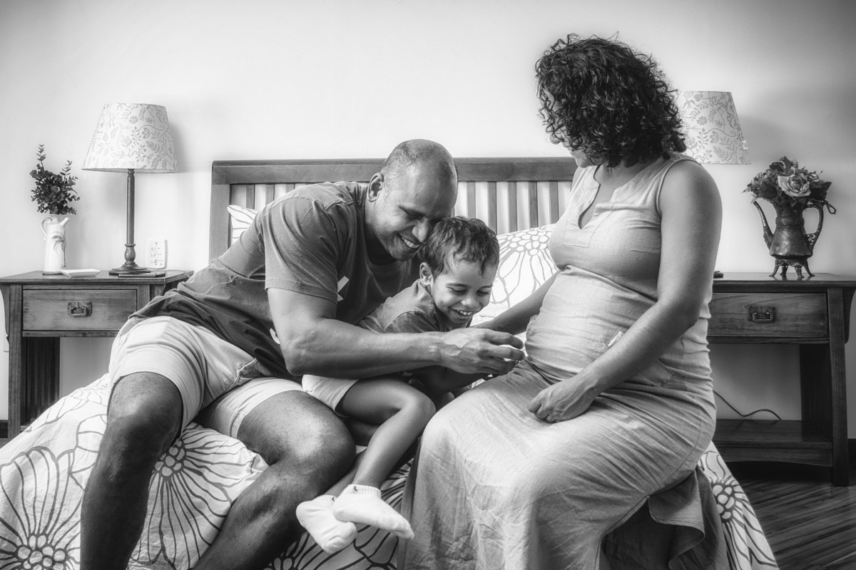 Pai, mãe e filho brincando na cama.