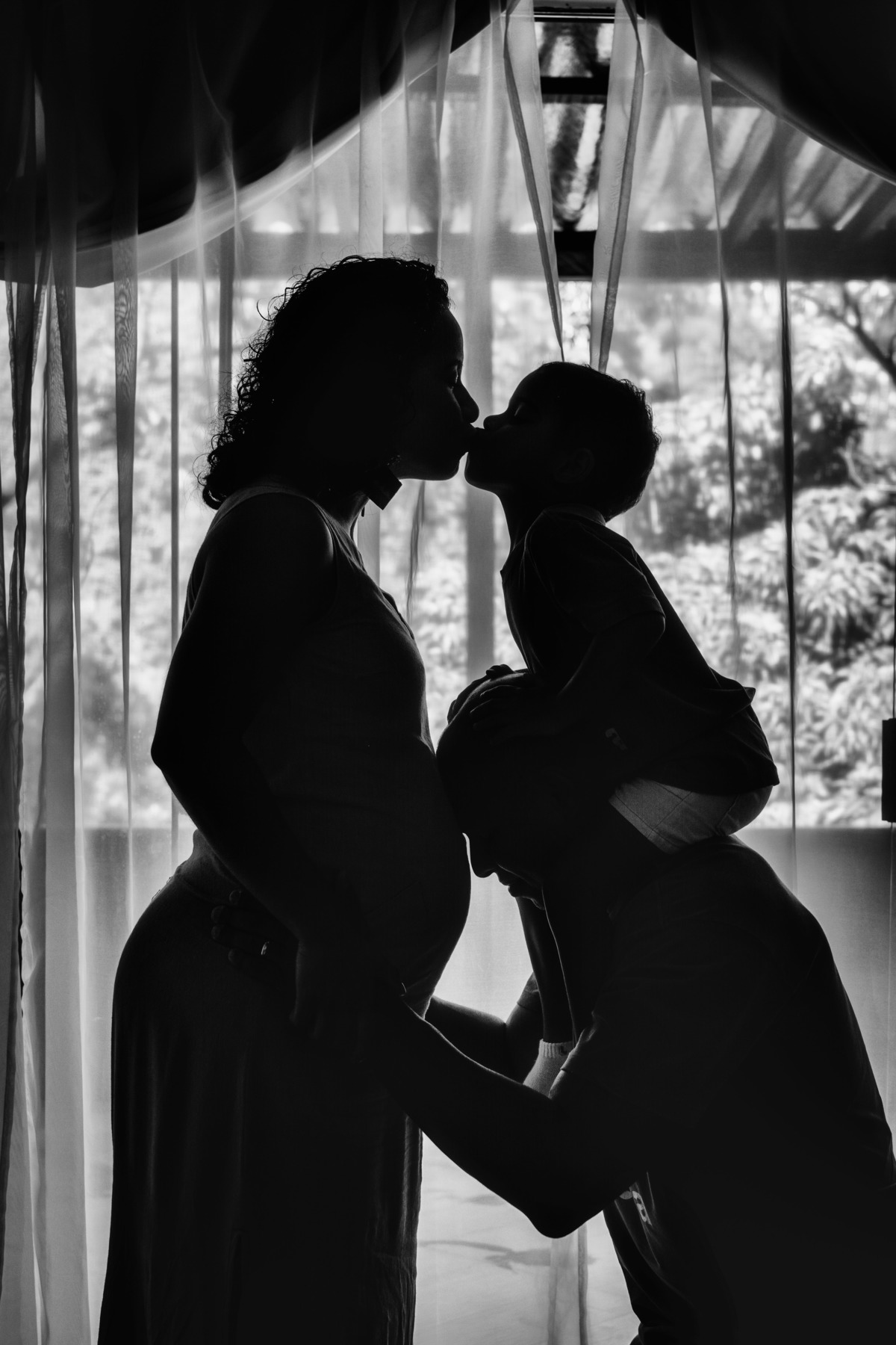 Silhueta de pai com filho na carcunda dando selinho na mãe grávida.