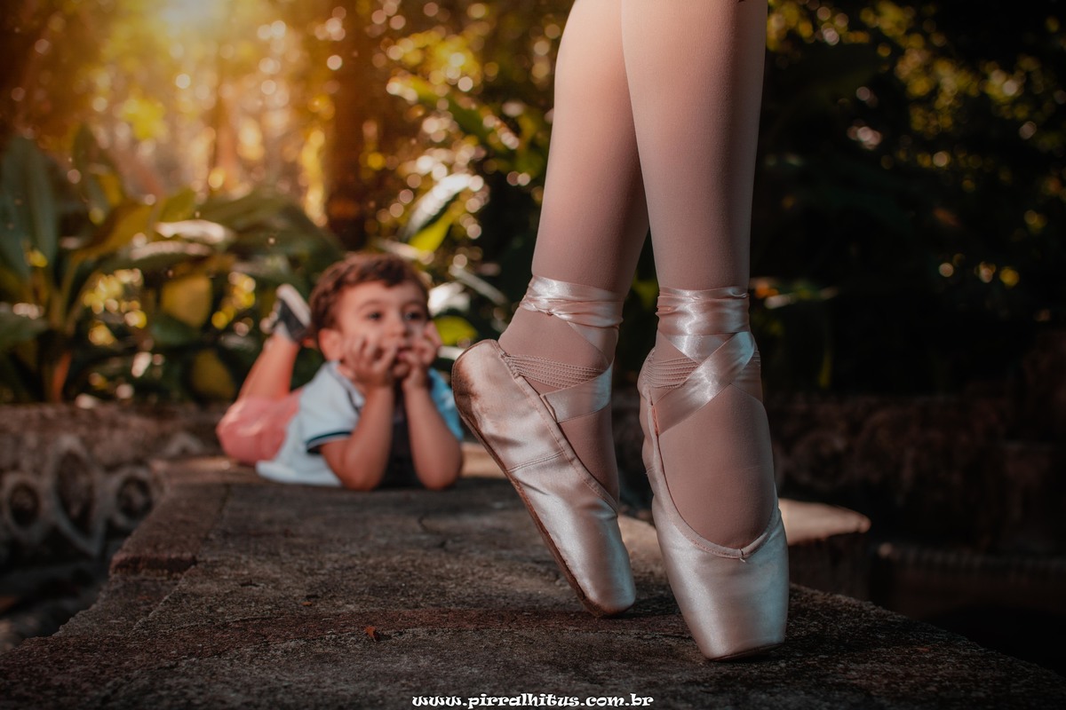 Menino observando a irmã bailarina fazendo ponta. Book fotográfico infantil no Parque Laje, Rio de Janeiro.