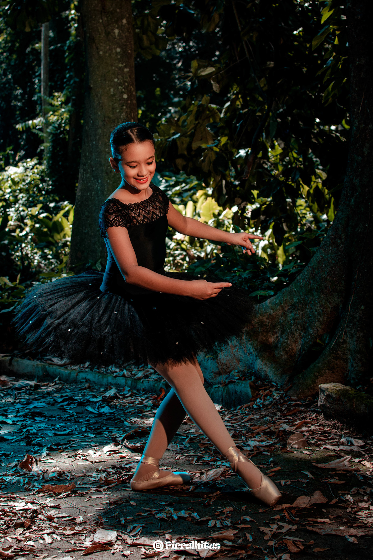 Pequena bailarina com collant bordado e tutu pretos fazendo passo de dança durante ensaio fotográfico infantil no Parque Laje, Rio de Janeiro.