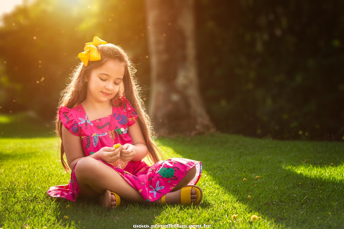 Menina com laço de fita amarela no cabelo e vestido rosa no Rio 2 Park.