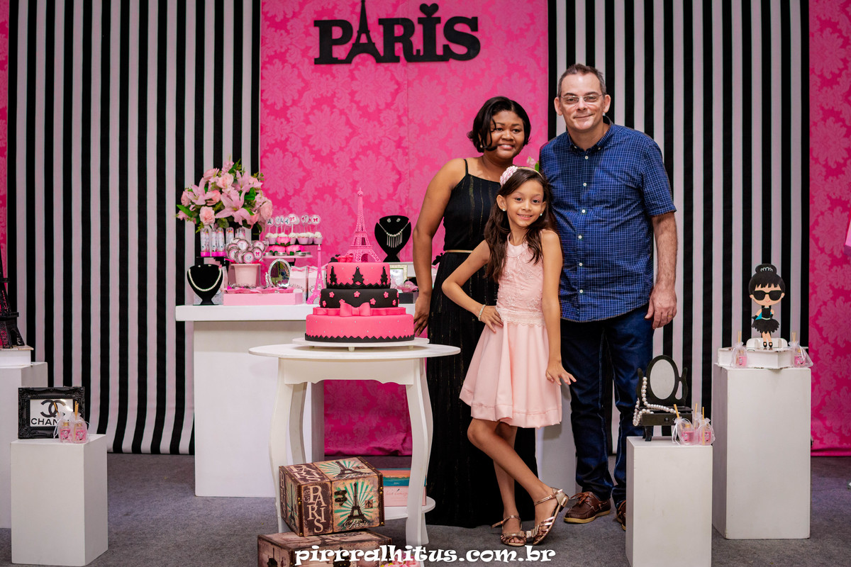 Aniversariante e seus pais na mesa do bolo.