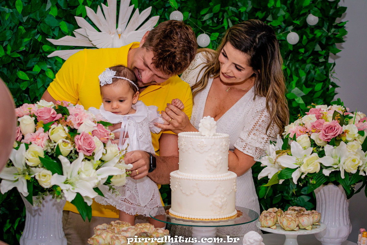 Pais com bebê na mesa do bolo em comemoração ao batizado.