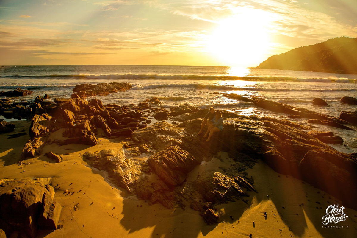 Noivos sentados à beira mar