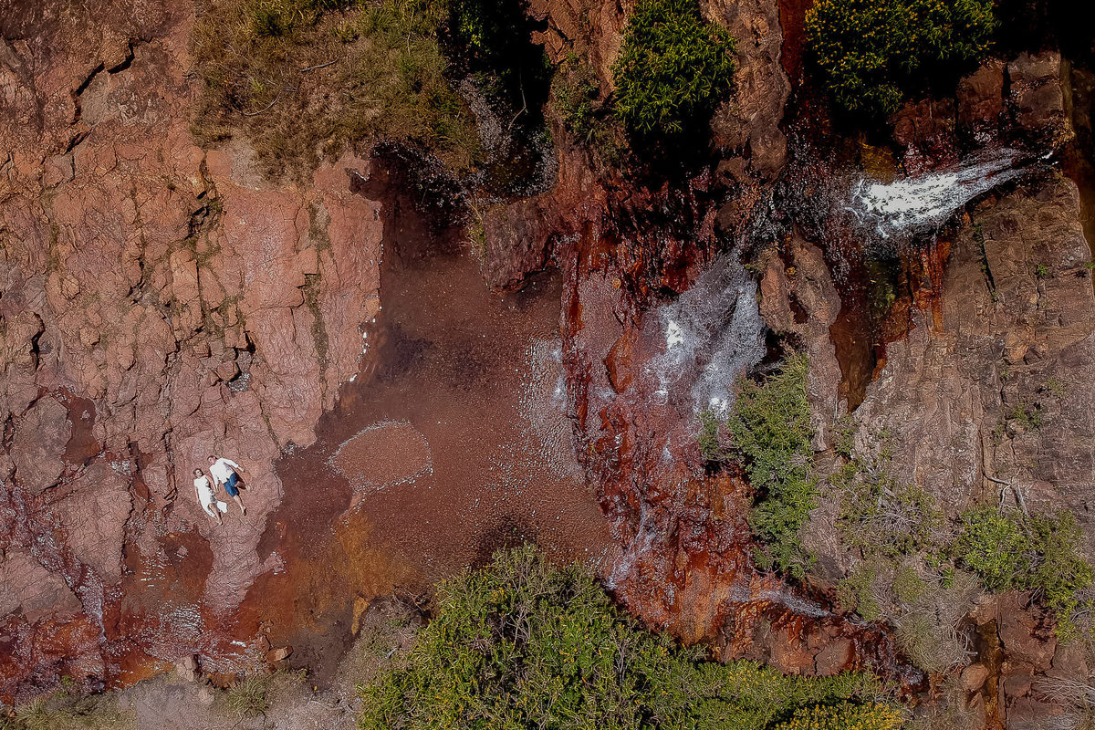 imagem aérea dos noivos deitados na pedra próximos a uma cascata