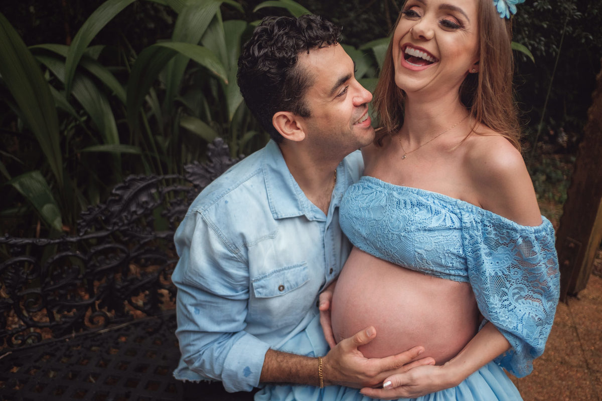 mamãe gestante sentada no colo do papai e dando gargalhada