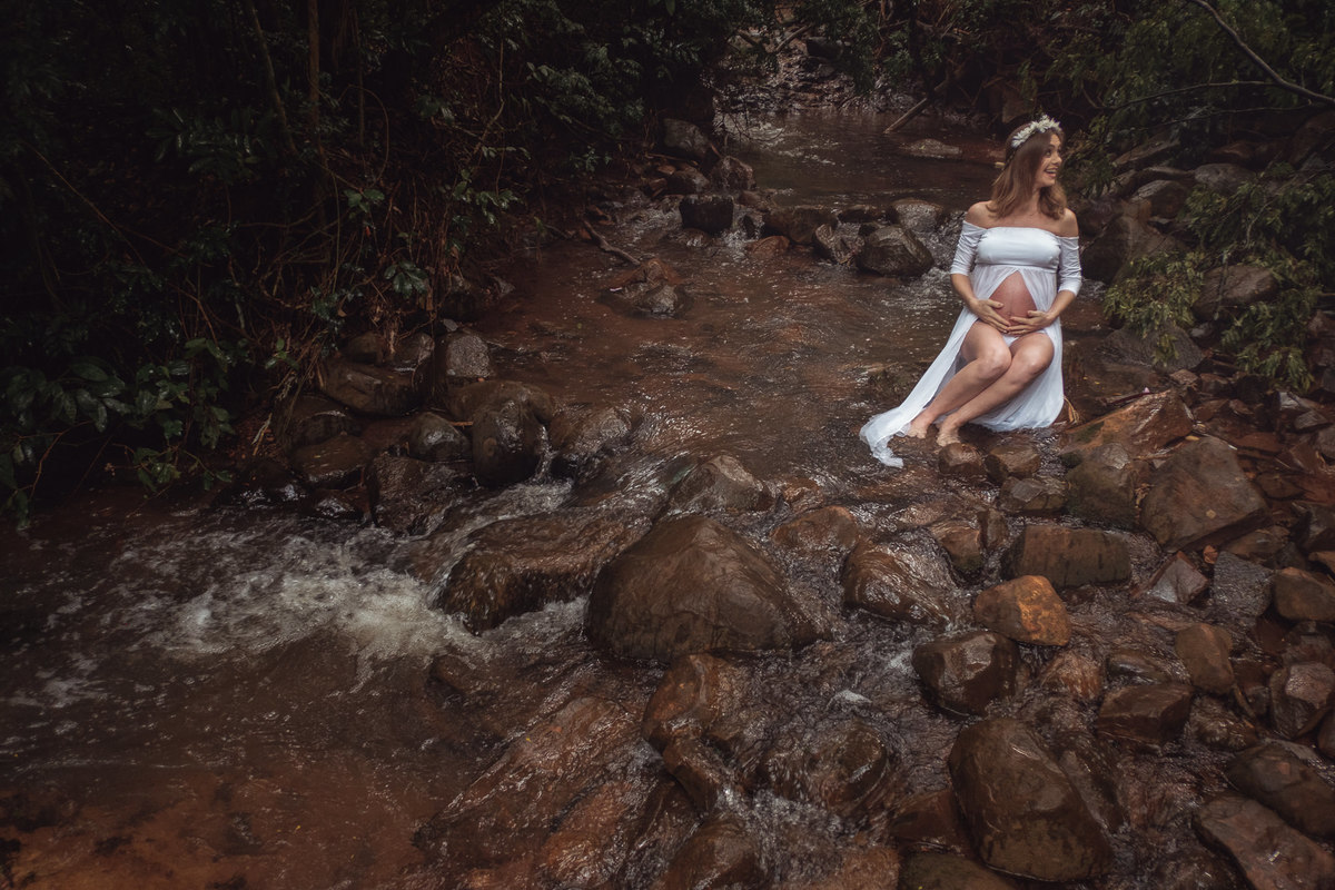 Mamãe gestante sentada nas pedras em meio a um córrego