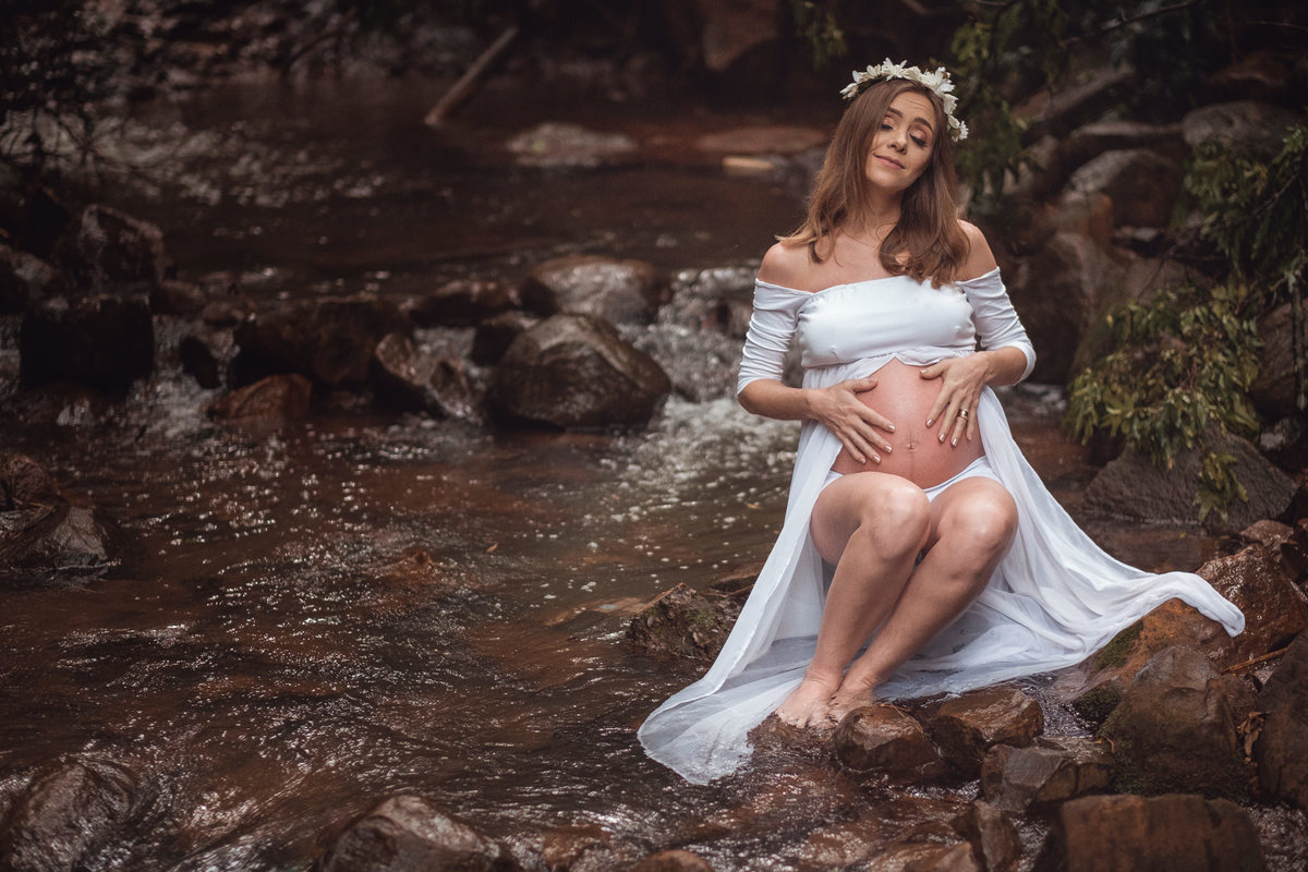 Mamãe gestante sentada nas pedras em meio a um córrego