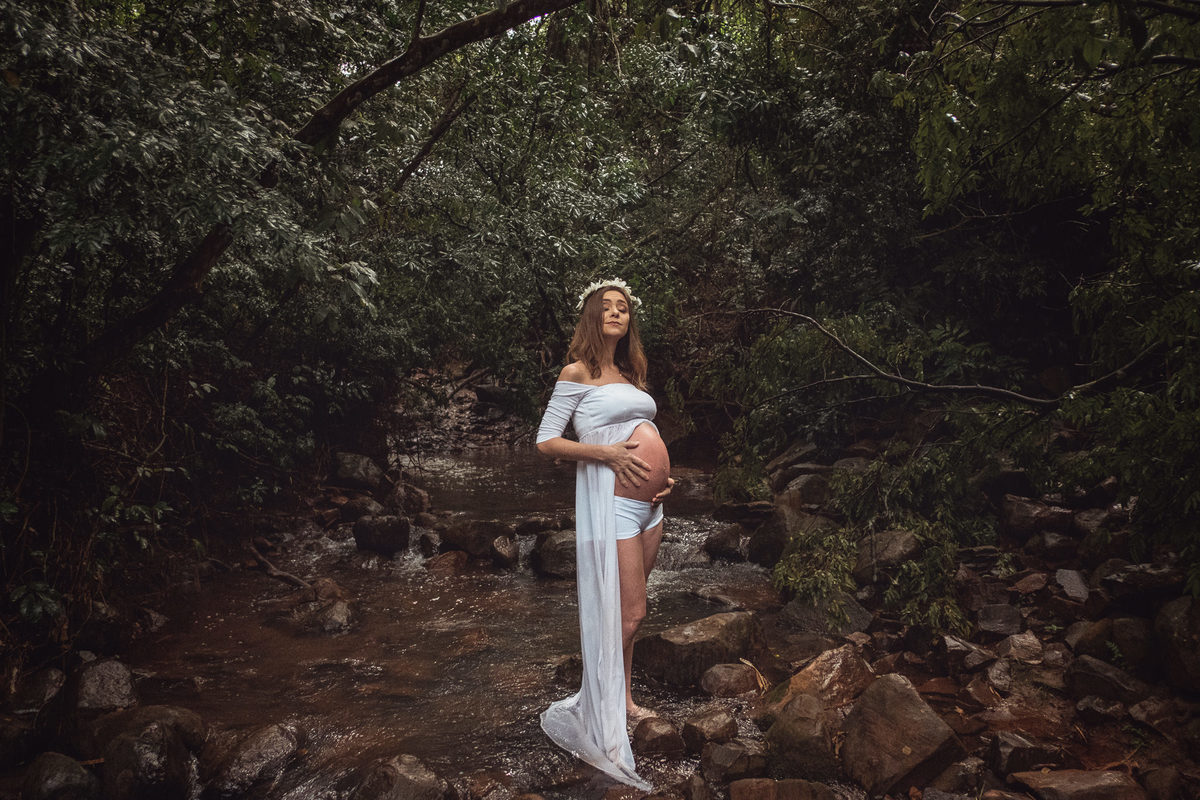 Mamãe gestante sentada nas pedras em meio a um córrego