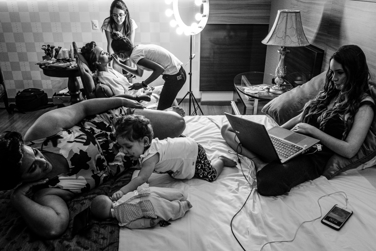 noiva se maquiando enquanto sua irmã está no notebook e sua mãe brinca com a daminha no making of